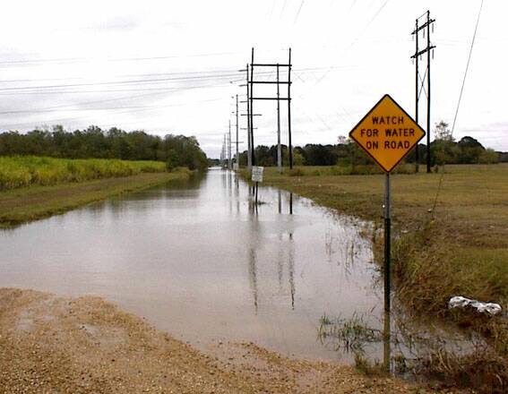 Straße mit Warnschild steht unter Wasser.
